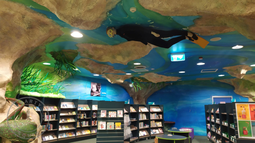 room with books. room has underwater theme. there is a dummy diver on the ceiling