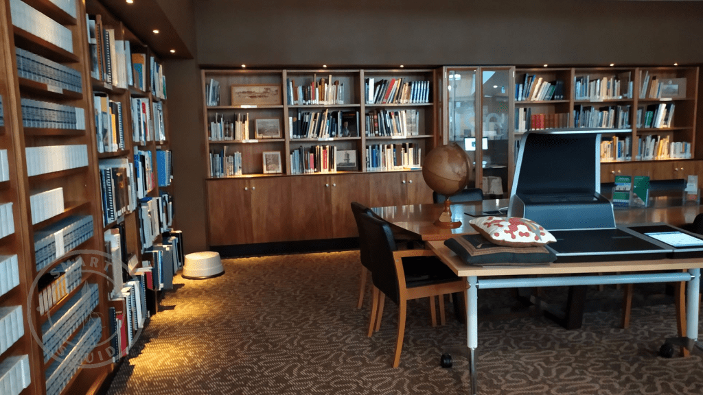 room with book shelves on the walls. there is a table in the middle of the room. there is a microfiche reader and globe on top the of the table