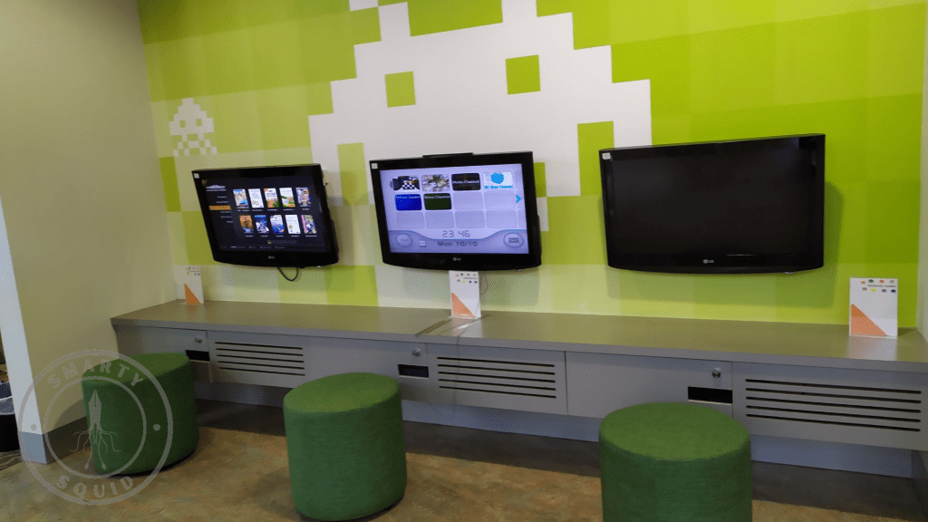 three tv monitors on the wall. green round seats in front of the monitors