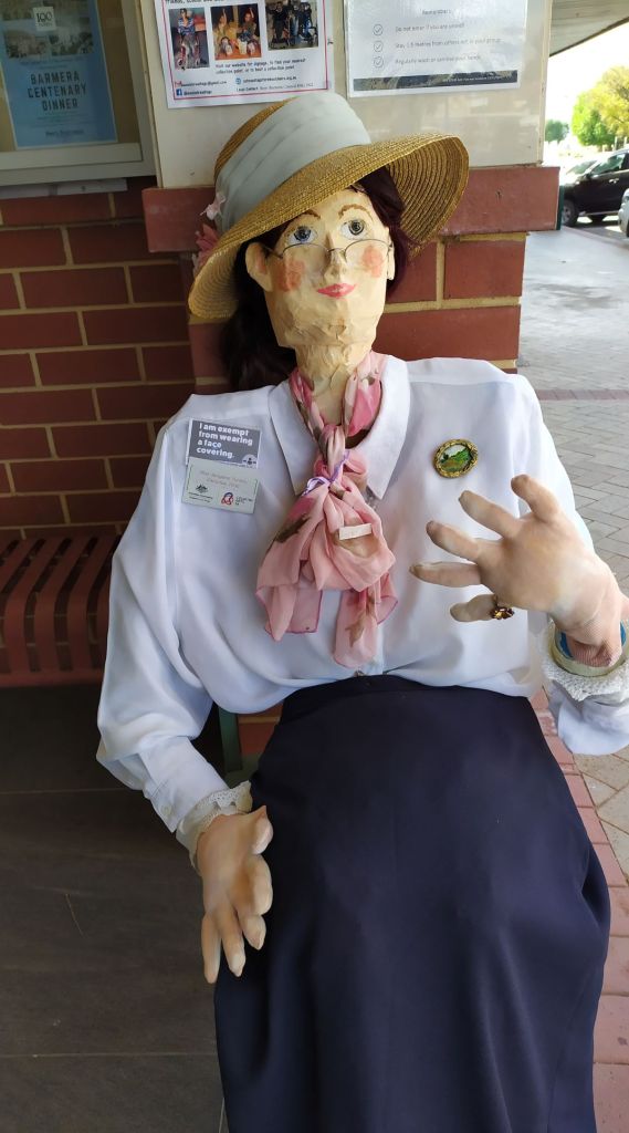 a dummy dressed in white blouse and blue skirt sitting on a chair outside a shop
