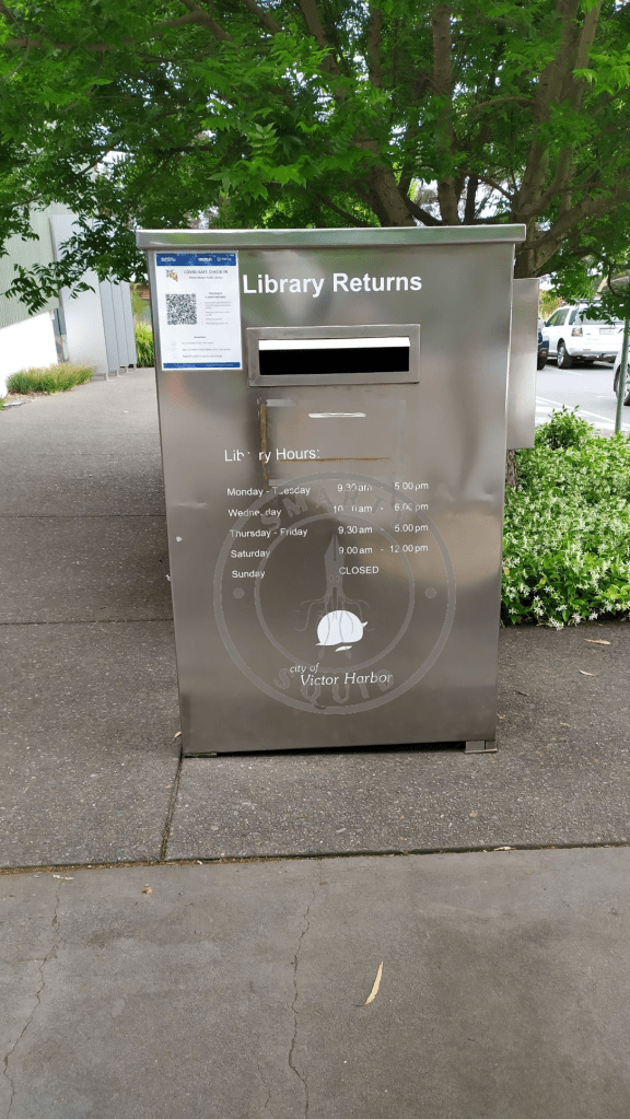 outside of the Victor Harbor Library looking at the a metallic box with a sign at the fron saying Library Returns